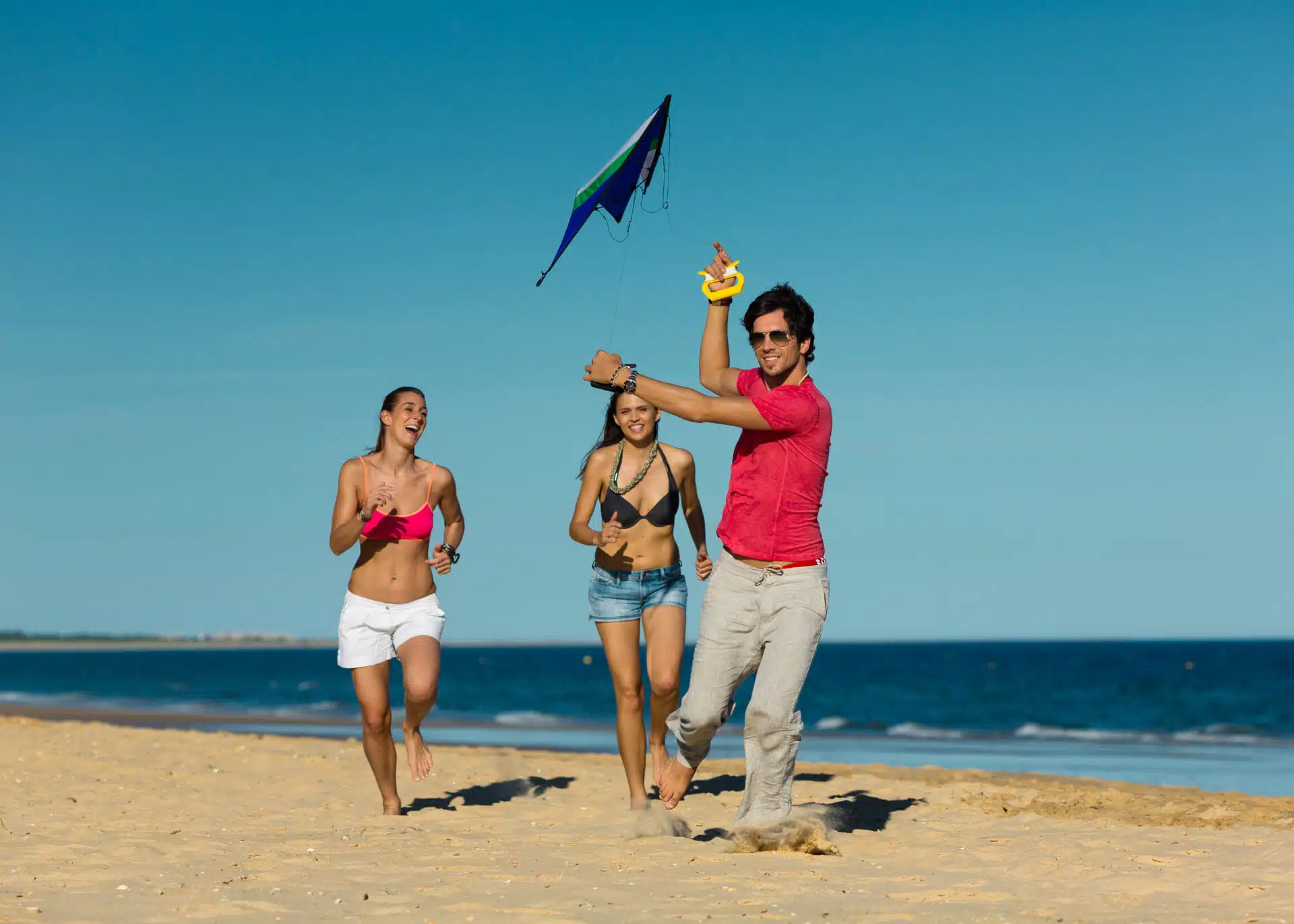 man and two women running on beach with kite