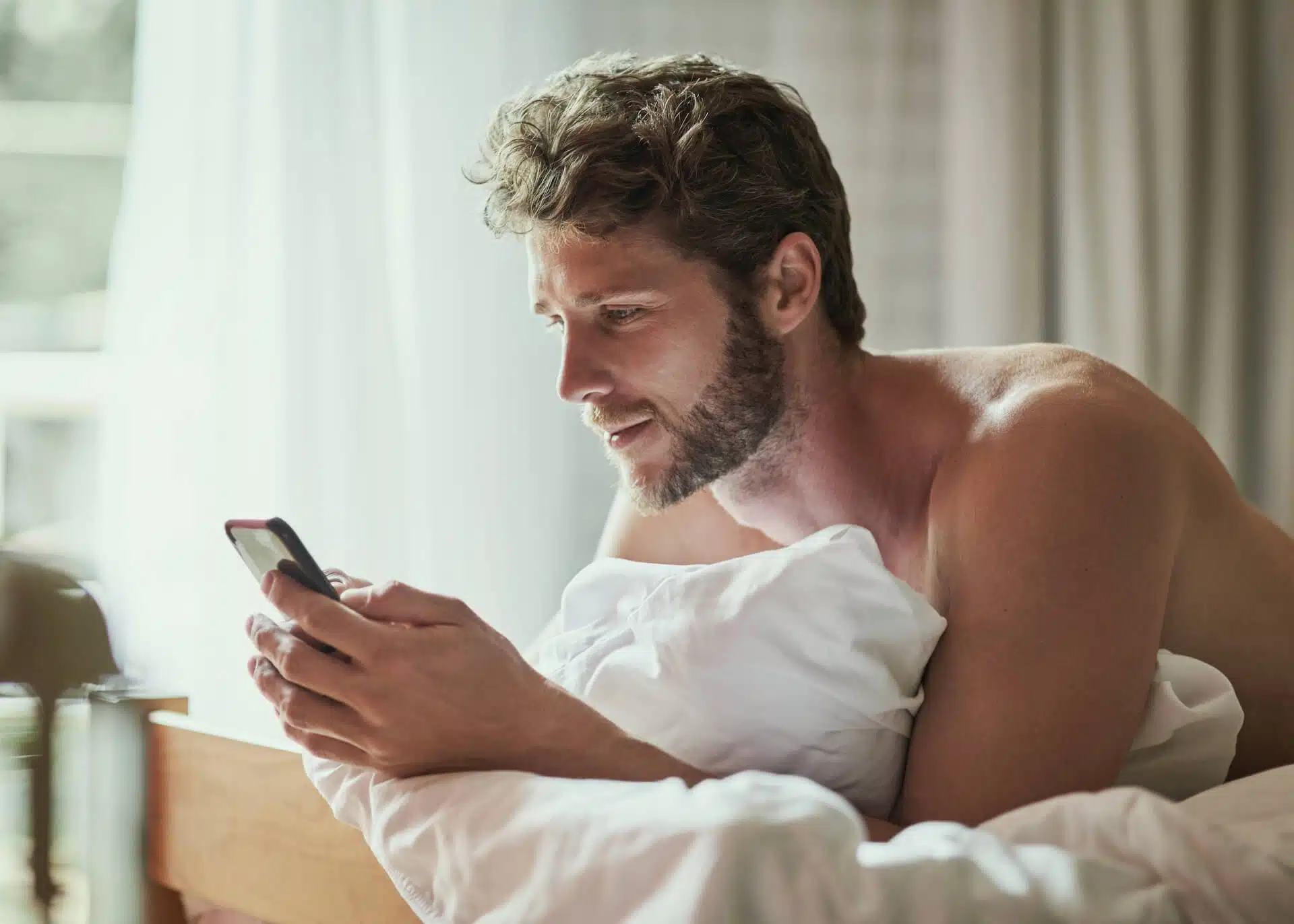 handsome young man texting on his phone in bed