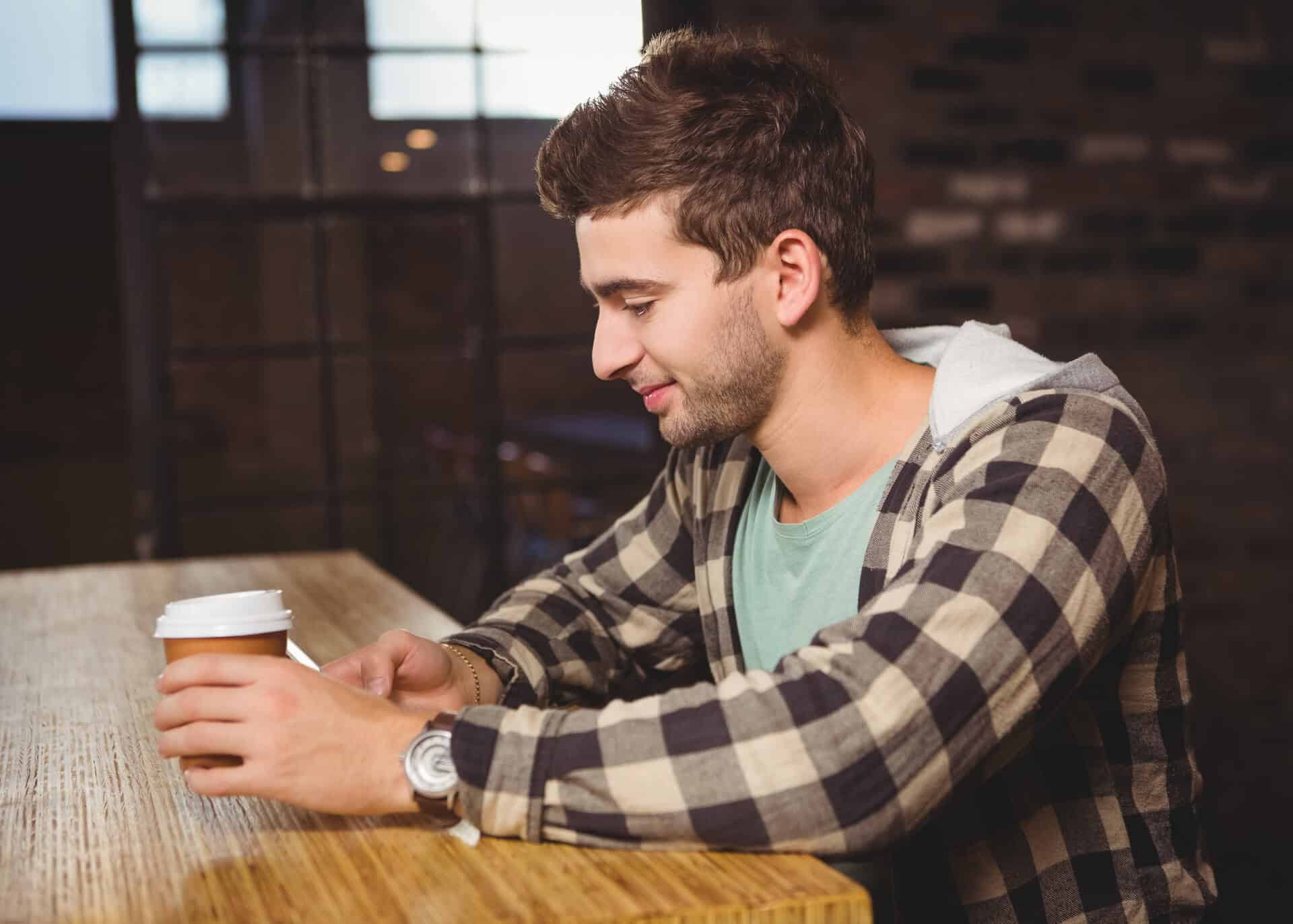 smiling guy texting while holding coffee cup