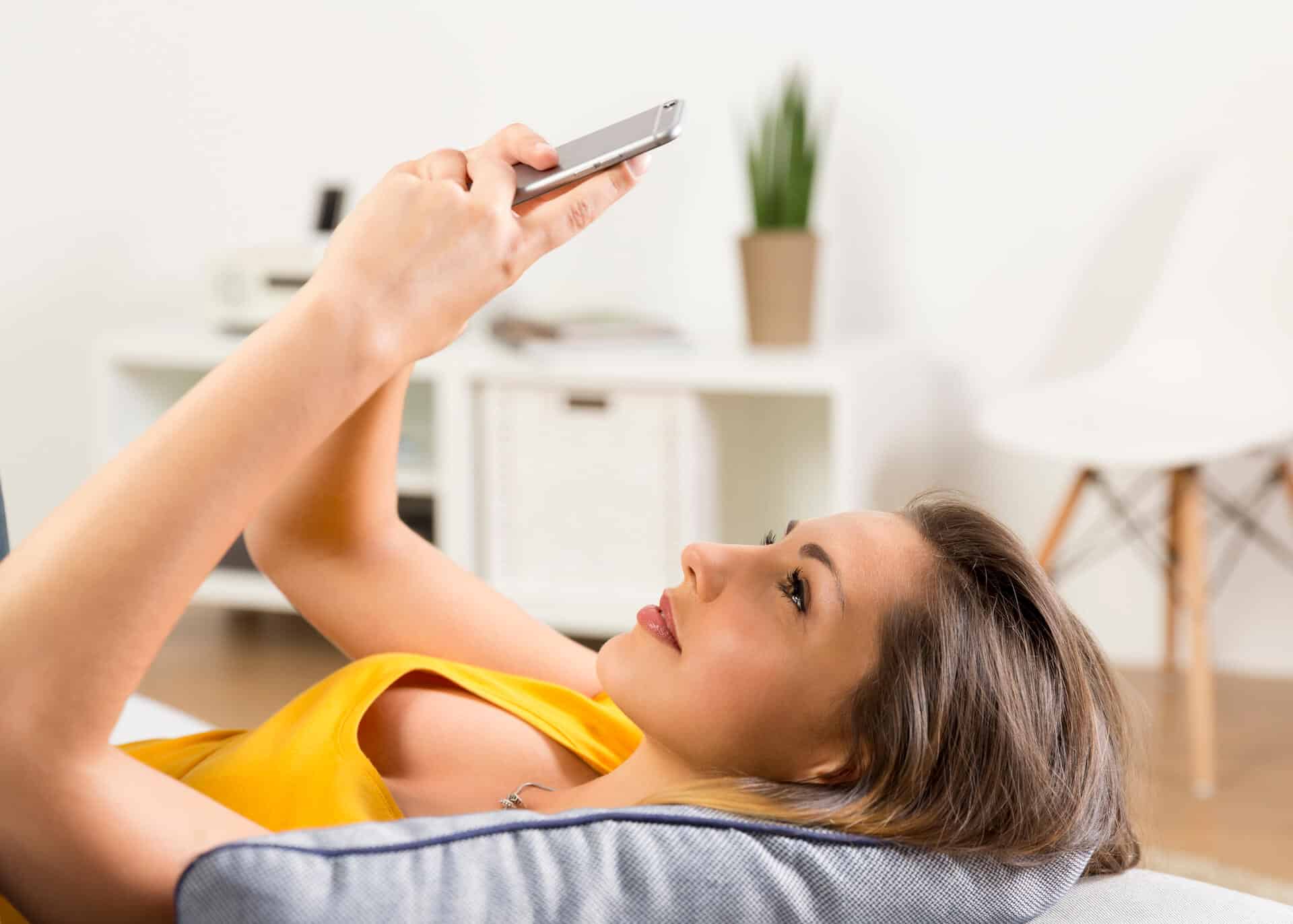 smiling woman laying on couch texting
