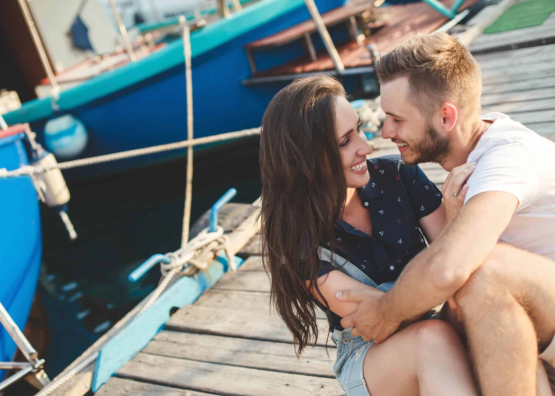 guy and girl sitting on wooden pier holding hands and laughing