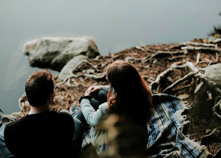 two people sitting on a cliff talking