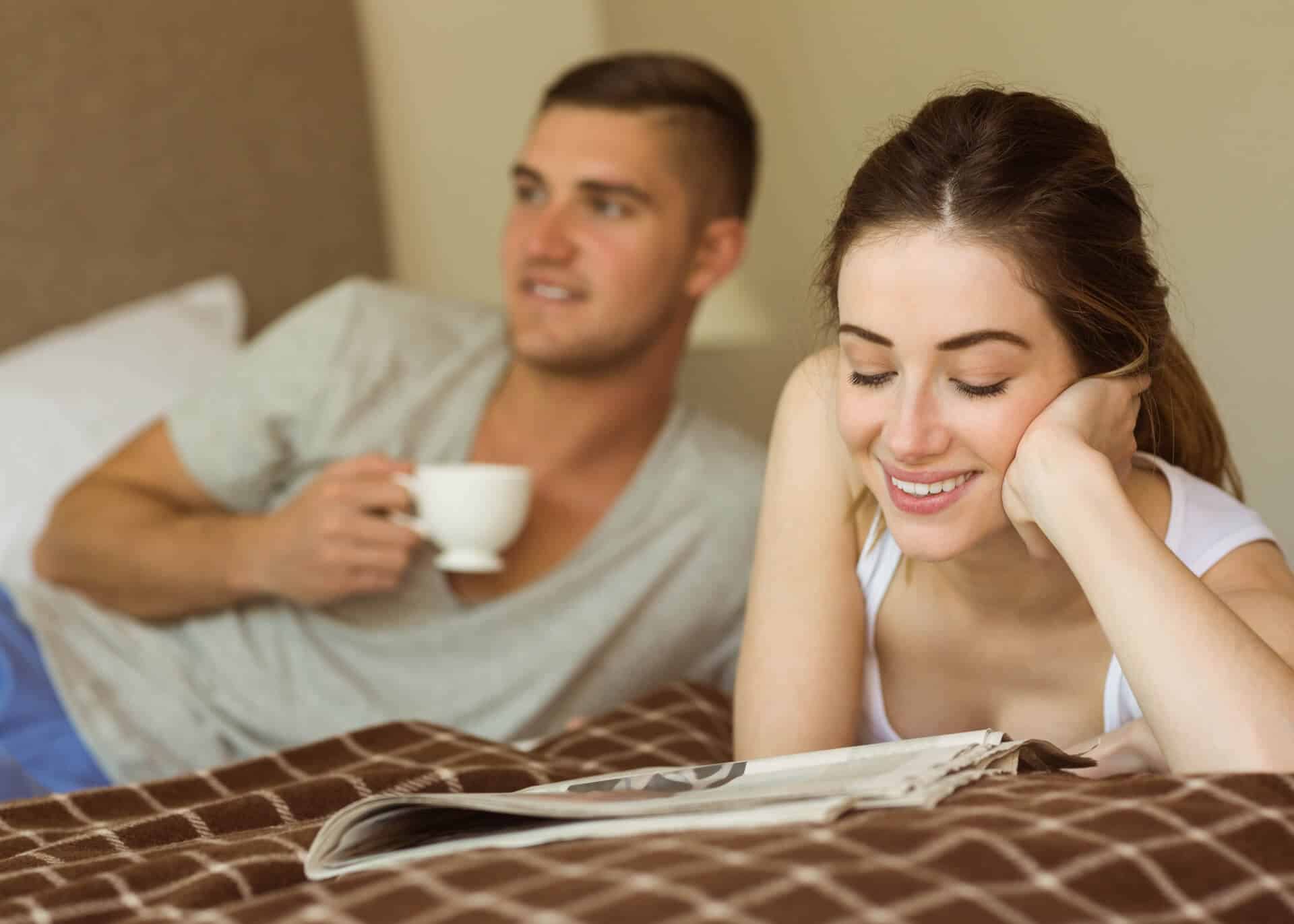 young couple reading newspaper in bed