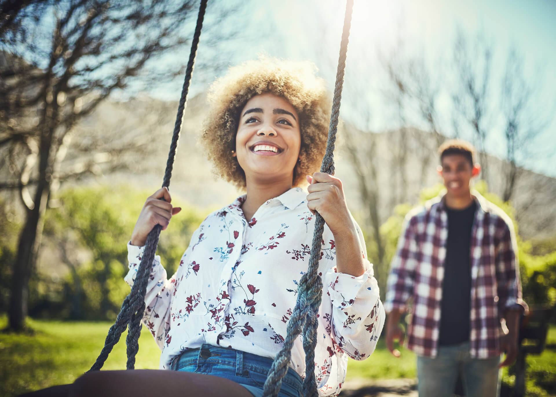 young woman on a swing with her boyfriend standing behind